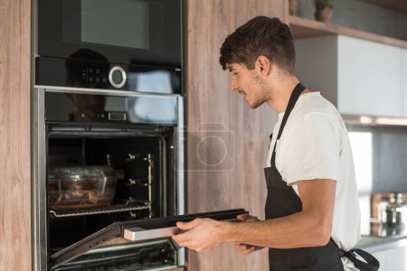 Téléchargez les photos : "homme ouvrant le four dans la cuisine de la maison
" - en image libre de droit