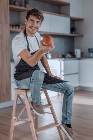 Foto de "atractivo hombre con una manzana sentado en una cocina casera
" - Imagen libre de derechos
