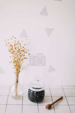 Photo for "Dry black tea in glass jar and honey spindle on kitchen background. Hot drink in cold period" - Royalty Free Image