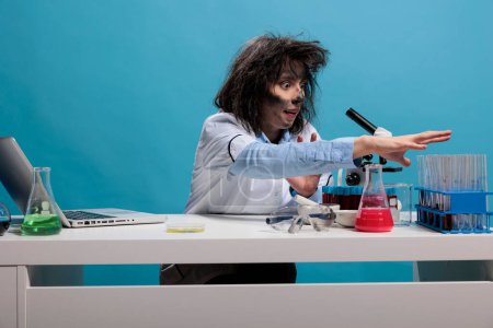Téléchargez les photos : Crazy scientist with goofy look grabbing glass test tubes sitting in rack while working in laboratory. - en image libre de droit