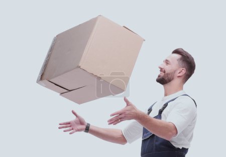 Foto de "Vista lateral. hombre sonriente en overoles atrapa una caja de cartón" - Imagen libre de derechos