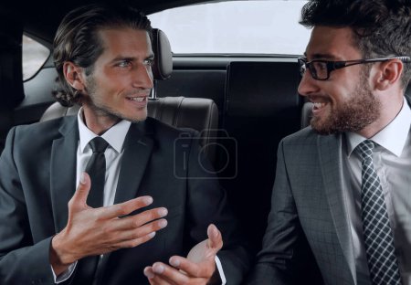 Téléchargez les photos : Deux hommes d'affaires parlant assis dans la voiture - en image libre de droit