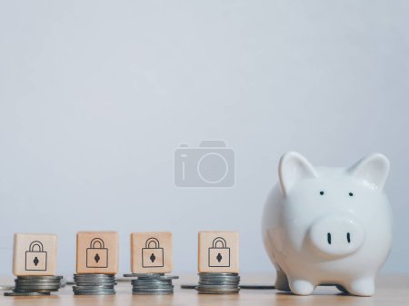 Photo for "White piggy bank near stack coins with wooden padlock block on top on table to security of money invest for future. Concept for loan, property ladder, financial,real estate investment,taxes and bonus." - Royalty Free Image