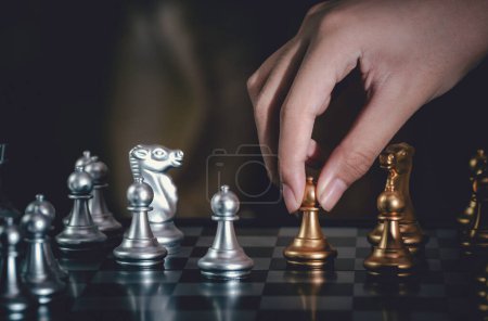Photo for "Hand businessman moving silver pawn chess fighting on board with gold chess background. successfully in the competition with technology network background. Management or leadership strategy concept." - Royalty Free Image
