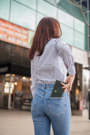 Foto de "Mujer confiada posando en guardar guardando su billetera en el bolsillo trasero" - Imagen libre de derechos