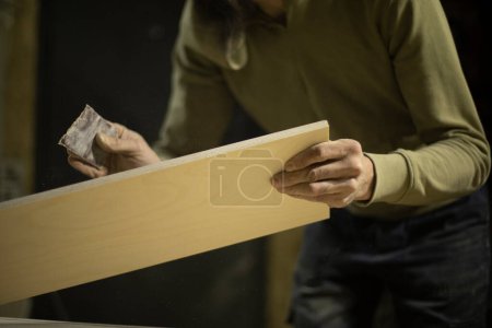 Photo for "Carpenter grinds board. Man creates furniture. Hands hold sanding paper." - Royalty Free Image