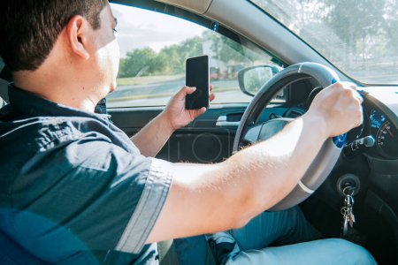Photo for "Person holding the cell phone and with the other hand the steering wheel, Man using his phone while driving, Concept of irresponsible driving, Distracted driver using the cell phone while driving" - Royalty Free Image