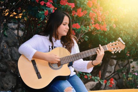 Foto de "Portrait of a smiling girl playing guitar, A girl sitting playing guitar outdoors, Lifestyle of a girl playing guitar outdoors" - Imagen libre de derechos
