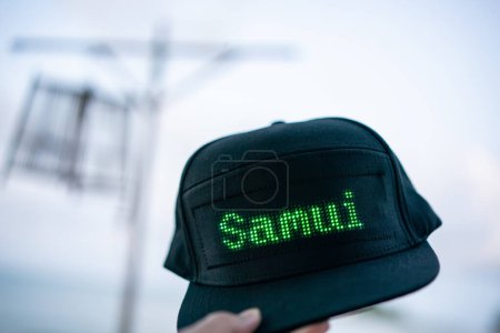 Téléchargez les photos : "Main tenant casquette de baseball noire avec lettre LED "" Samui "", vacances d'été." - en image libre de droit