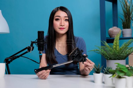 Téléchargez les photos : "Asian vlogger creator holding professional tripod reviewing vlogging product" - en image libre de droit