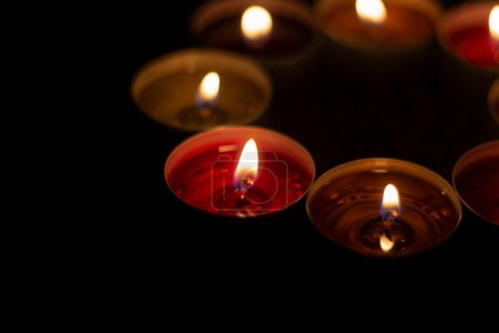 Téléchargez les photos : "Les bougies rondes brûlent dans l'obscurité. Bougies à la cire sur fond sombre. Feux rouges et jaunes." - en image libre de droit