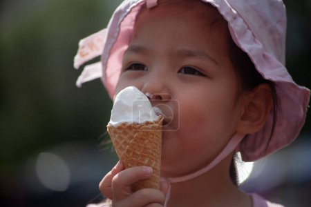 Photo for "The child is eating ice cream. Girl licking ice cream on the street. A waffle cone in the hands of an Asian child." - Royalty Free Image
