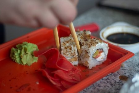 Téléchargez les photos : "Sushi au poisson et riz. Nourriture du restaurant. Prend des sushis avec des bâtons de bois. Nourriture du restaurant chinois. Cuisine orientale. Livraison du déjeuner à la maison." - en image libre de droit