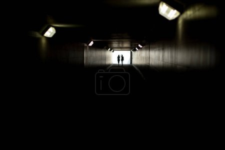 Téléchargez les photos : "Deux silhouettes au bout du tunnel. Lumière à distance. Chiffres de petites femmes à la lumière contrastée." - en image libre de droit
