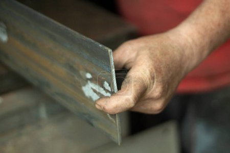 Téléchargez les photos : "Travailleur du métal. Il tient une pièce en acier. Travail acharné dans un atelier de métallurgie. Création de la construction métallique." - en image libre de droit
