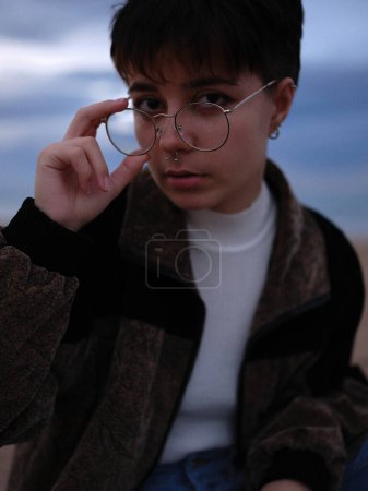 Photo for "young trans woman taking off her glasses while looking intently at the camera" - Royalty Free Image