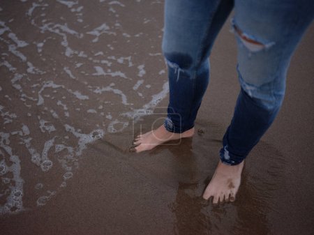 Photo for View from above of a person's legs with wet feet on the beach shore - Royalty Free Image