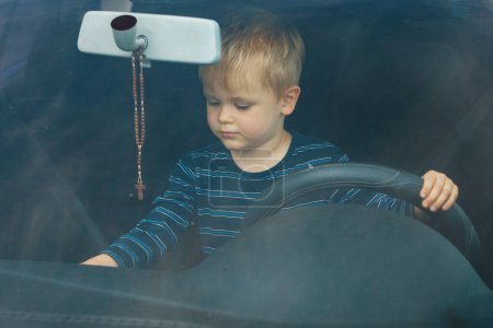 Téléchargez les photos : "Un petit garçon sérieux assis dans la voiture. L'enfant au volant." - en image libre de droit