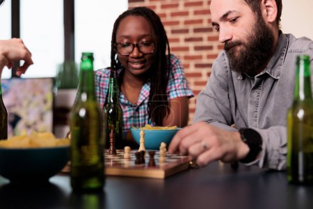 Téléchargez les photos : Smart multiethnic friends sitting at home while playing chess together. - en image libre de droit