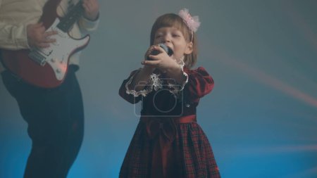 Téléchargez les photos : Little girl in vintage dress sings on stage, her father plays an electric guitar - en image libre de droit
