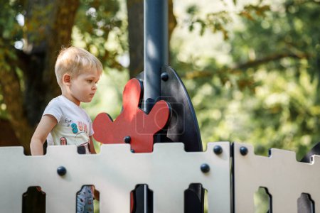 Téléchargez les photos : "Petit garçon tournant la barre d'un bateau-jouet dans une aire de jeux pour enfants avec confiance." - en image libre de droit