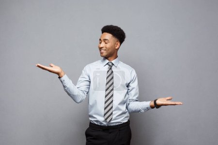 Téléchargez les photos : "Concept d'affaires - Confiant réfléchi jeune Afro-Américain montrant les mains équilibrées sur le côté sur fond gris
." - en image libre de droit