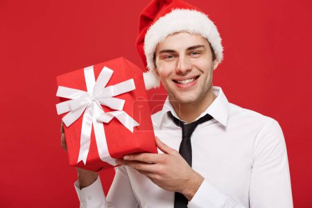 Téléchargez les photos : "Concept de Noël - portrait close-up Père Noël homme d'affaires sur fond rouge tenant cadeau rouge
." - en image libre de droit
