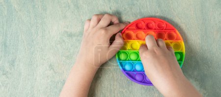 Photo for "banner with Kid playing with pop it sensory toy. boy pressing on colorful rainbow squishy soft silicone bubbles. Stress and anxiety relief. Trendy fidgeting game" - Royalty Free Image