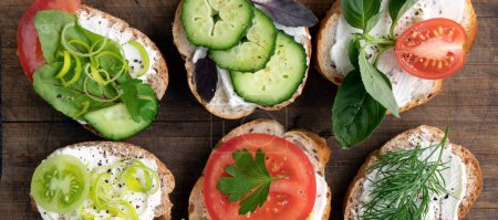 Photo for Banner with various vegetable sandwiches with cream cheese, tomatoes, dill, cucumbers, leeks and basil. serving a vegetarian sandwiches for appetizers on cutting board. top view - Royalty Free Image
