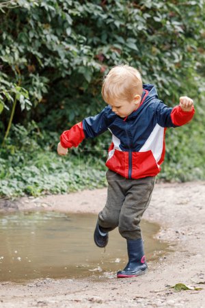 Téléchargez les photos : "Petit garçon éclaboussant dans une flaque de boue, sautant dans une flaque" - en image libre de droit