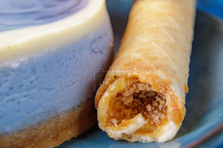 Téléchargez les photos : "Gâteau au fromage avec des myrtilles et des tubes de confiserie avec du lait concentré sur une assiette bleue. Gros plan" - en image libre de droit