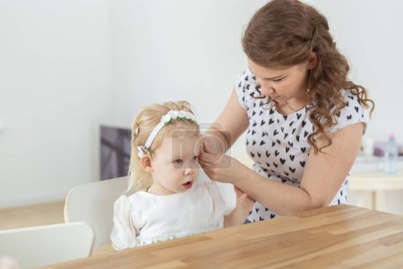 Photo for "Mother helps to put on cochlear implant for her deaf little daughter. Hearing aid and deafness concept" - Royalty Free Image