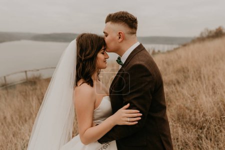 Téléchargez les photos : "couple mariage jeunes mariés dans un câlin de marche embrasser sur l'herbe haute sur la montagne au-dessus de la rivière" - en image libre de droit
