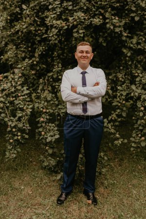 Photo for "successful businessman groom in classic clothes stands his hands clasped together in nature" - Royalty Free Image