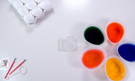 Photo for "Tools for painting eggs for easter, eggs box, cups of colorful paint, easter eggs, plate, brushes and paints on the table side view" - Royalty Free Image