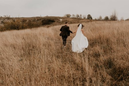 Téléchargez les photos : "couple mariage jeunes mariés marcher courir sur l'herbe haute sur la montagne au-dessus de la rivière" - en image libre de droit