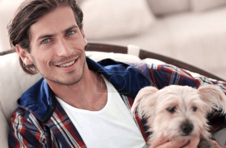 Photo for "handsome guy stroking his dog while sitting in a large armchair." - Royalty Free Image
