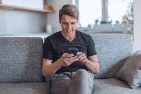 Téléchargez les photos : "souriant jeune homme lisant de la correspondance sur son smartphone
" - en image libre de droit