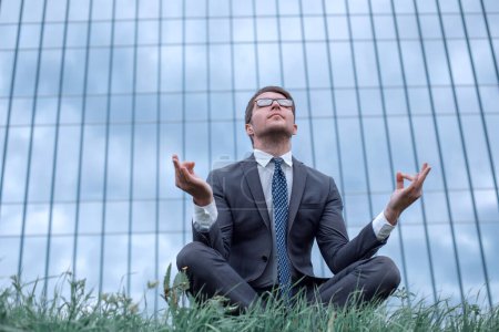 Foto de "hombre de negocios en Lotus pose sentado en la hierba frente al edificio de oficinas
" - Imagen libre de derechos