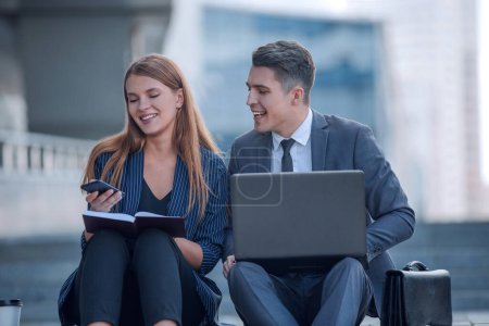 Téléchargez les photos : Jeune couple d'affaires lecture nouvelles en ligne près de l'immeuble de bureaux - en image libre de droit