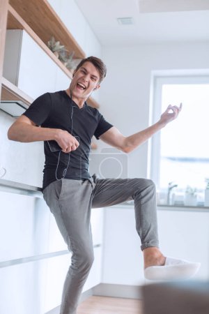 Téléchargez les photos : Heureux jeune homme avec smartphone chante dans sa cuisine - en image libre de droit