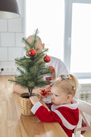 Photo for Child with cochlear implant hearing aid having fun with father and small christmas tree - diversity and deafness treatment and medical innovative technologies - Royalty Free Image