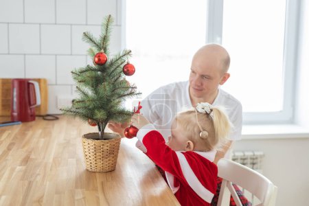 Photo for "Child with cochlear implant hearing aid having fun with father and small christmas tree - diversity and deafness treatment and medical innovative technologies" - Royalty Free Image