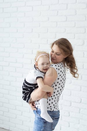 Téléchargez les photos : Mère tient son enfant avec des appareils auditifs et des implants cochléaires sur un mur de briques blanches. Sourds et diversité et concept de santé - en image libre de droit