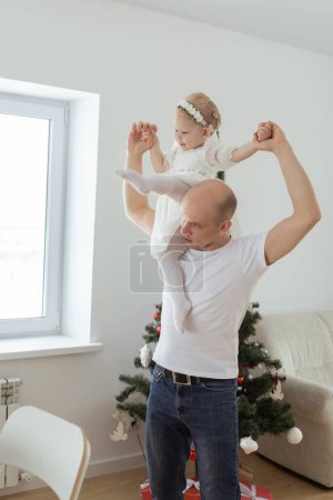 Téléchargez les photos : Bébé enfant avec prothèse auditive et implant cochléaire s'amusant avec son père sur fond d'arbre de Noël. Sourds, diversité et santé concept - en image libre de droit