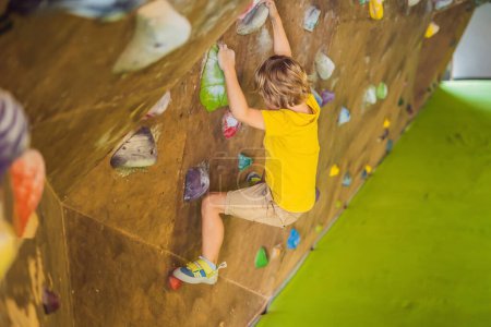 Foto de Niño pequeño escalando una pared de roca con botas especiales. interior - Imagen libre de derechos