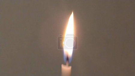 Téléchargez les photos : Longue même flamme d'une bougie solitaire sur un fond blanc foncé. - en image libre de droit