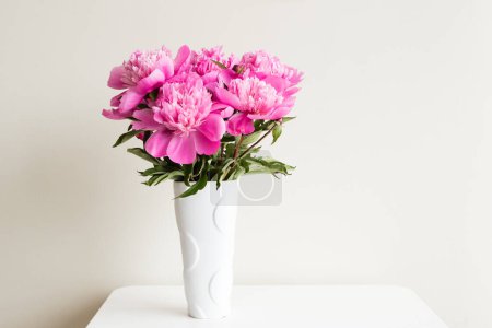 Photo for Pink peonies in white vase on table against neutral background - Royalty Free Image