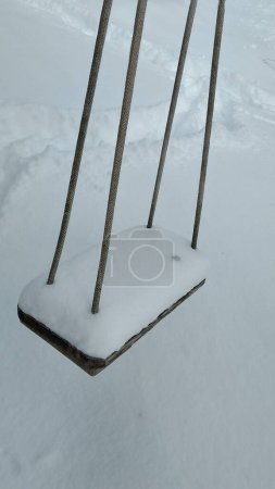 Photo for The children's wooden swing on four ropes is covered with snow. - Royalty Free Image