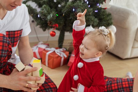 Foto de Niño pequeño con implante coclear juega con el padre bajo el árbol de navidad: sordera e innovadoras tecnologías médicas para audífonos - Imagen libre de derechos